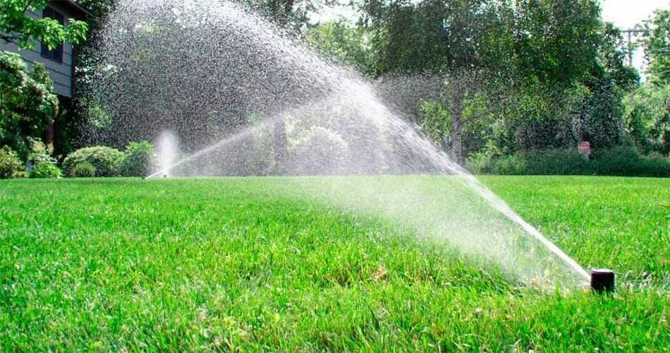 Automatic lawn sprinkler spraying water across a lush green lawn